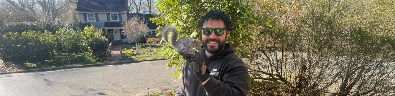 Technician in a hooded sweatshirt holding a squirrel outside a South Jersey home